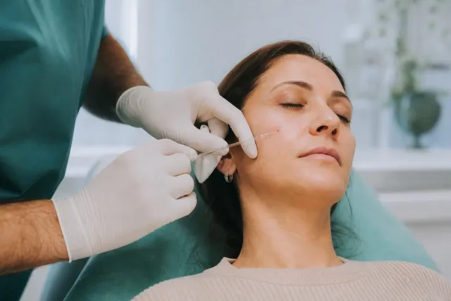 Mani guantate di un medico che eseguono un filler nella zona centrale del viso con una cannula sottile